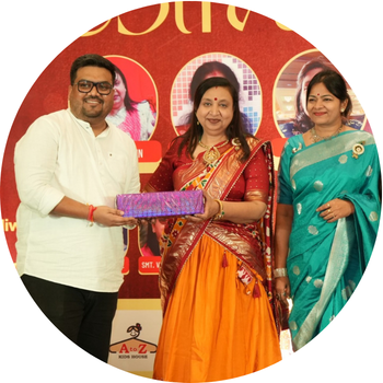 Man in a white short kurta presenting a wrapped gift box to a woman in a traditional yellow and red chaniya choli at a festive event.