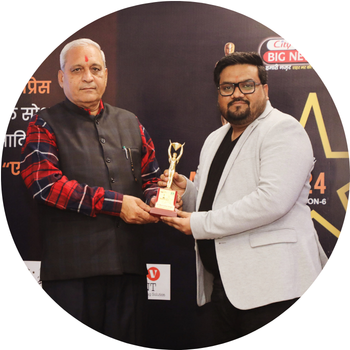 Man in a light grey blazer receiving a golden trophy award on stage from a senior dignitary in a dark vest at an award event hosted by Big News.