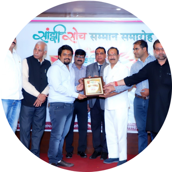 Man in a light blue shirt receiving a framed honor plaque on stage at Sanjhi Soch Samman Samaroh alongside committee members.