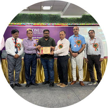 Man receiving a certificate of appreciation on stage at Om Sterling Global University flanked by university dignitaries and faculty members.