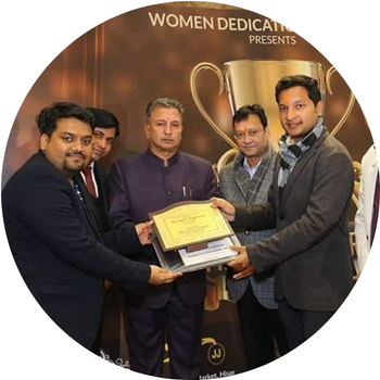 Group of men in formal blazers and suits jointly receiving a framed memento award at Women Dedication event backdrop in Hisar