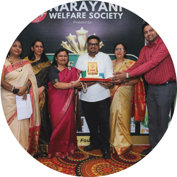Man in a white shirt receiving a golden award plaque on stage during Narayani Welfare Society event flanked by dignitaries in traditional attire.