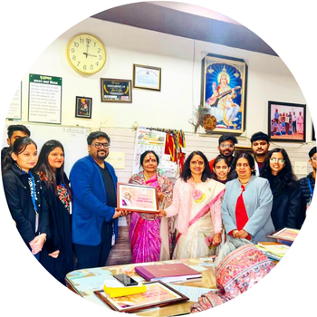 Man in a blue blazer receiving a framed portrait appreciation photo alongside guests inside an office setting